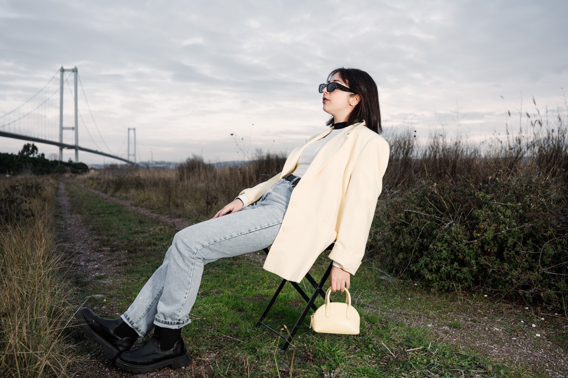 A stylish woman in sunglasses relaxes on a chair by a bridge in nature. — Achieving Your Dream Body: Miami's Premier Abdomino