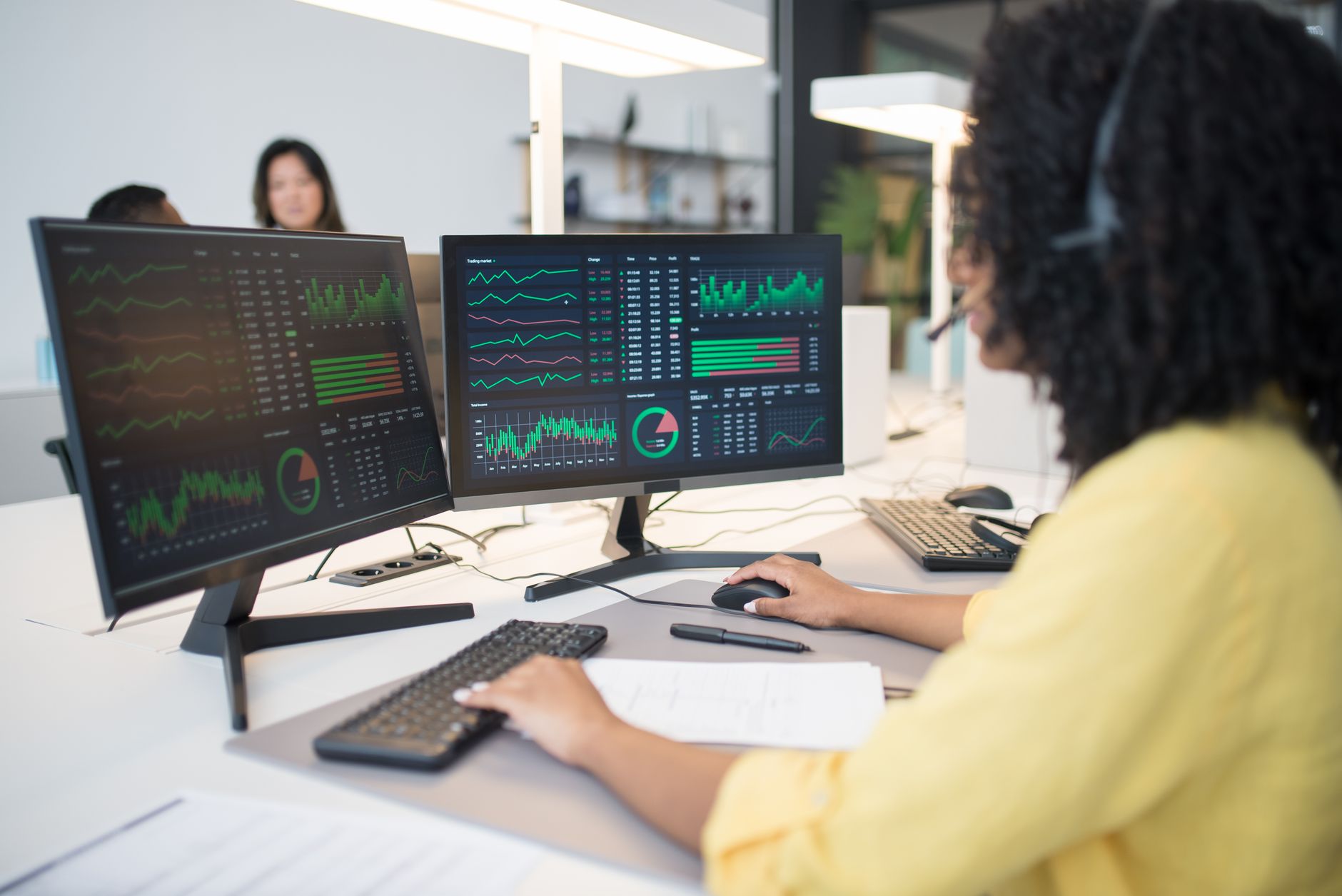 Woman analyzing financial data on dual screens at an office desk. — Take Profit Trader Helps You Focus on Strategy Over Stres